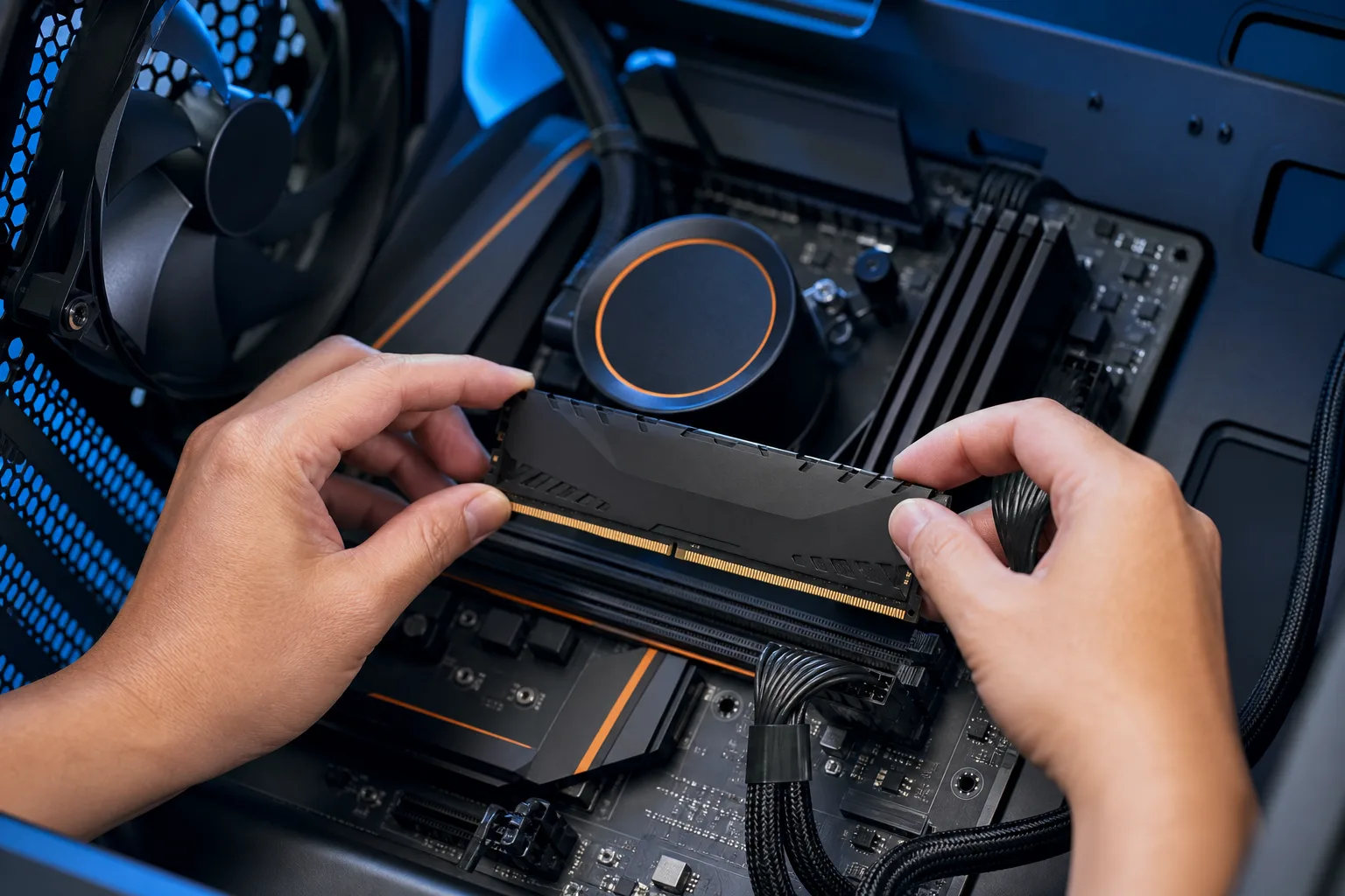 Two hands installing a black DDR RAM stick into a motherboard slot inside a blue-accented gaming PC with side panel removed.