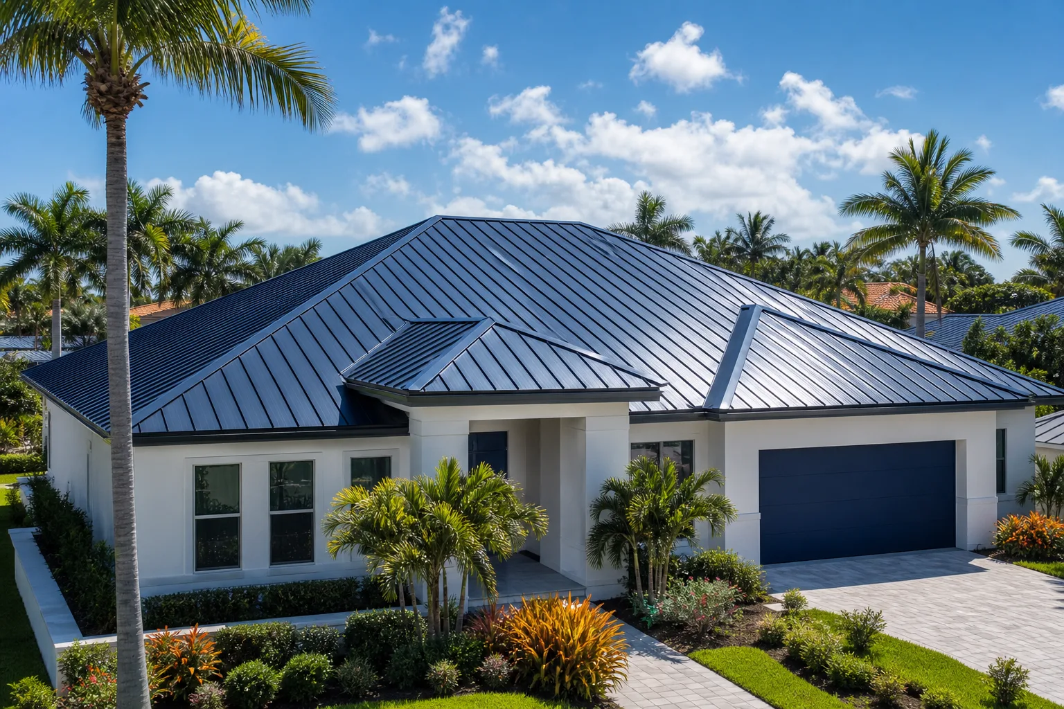 Modern white Florida home with dark standing-seam metal roof, palm trees, tropical landscaping, and paver driveway under blue sky.