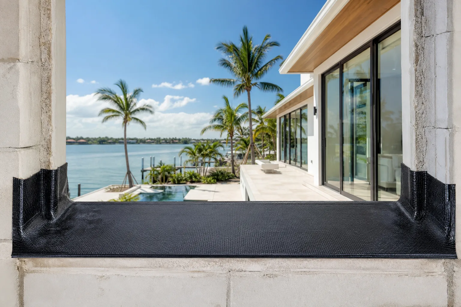 Close-up of a black self-adhering flexible flashing membrane sill pan installed in a concrete masonry window opening, waterfront home beyond